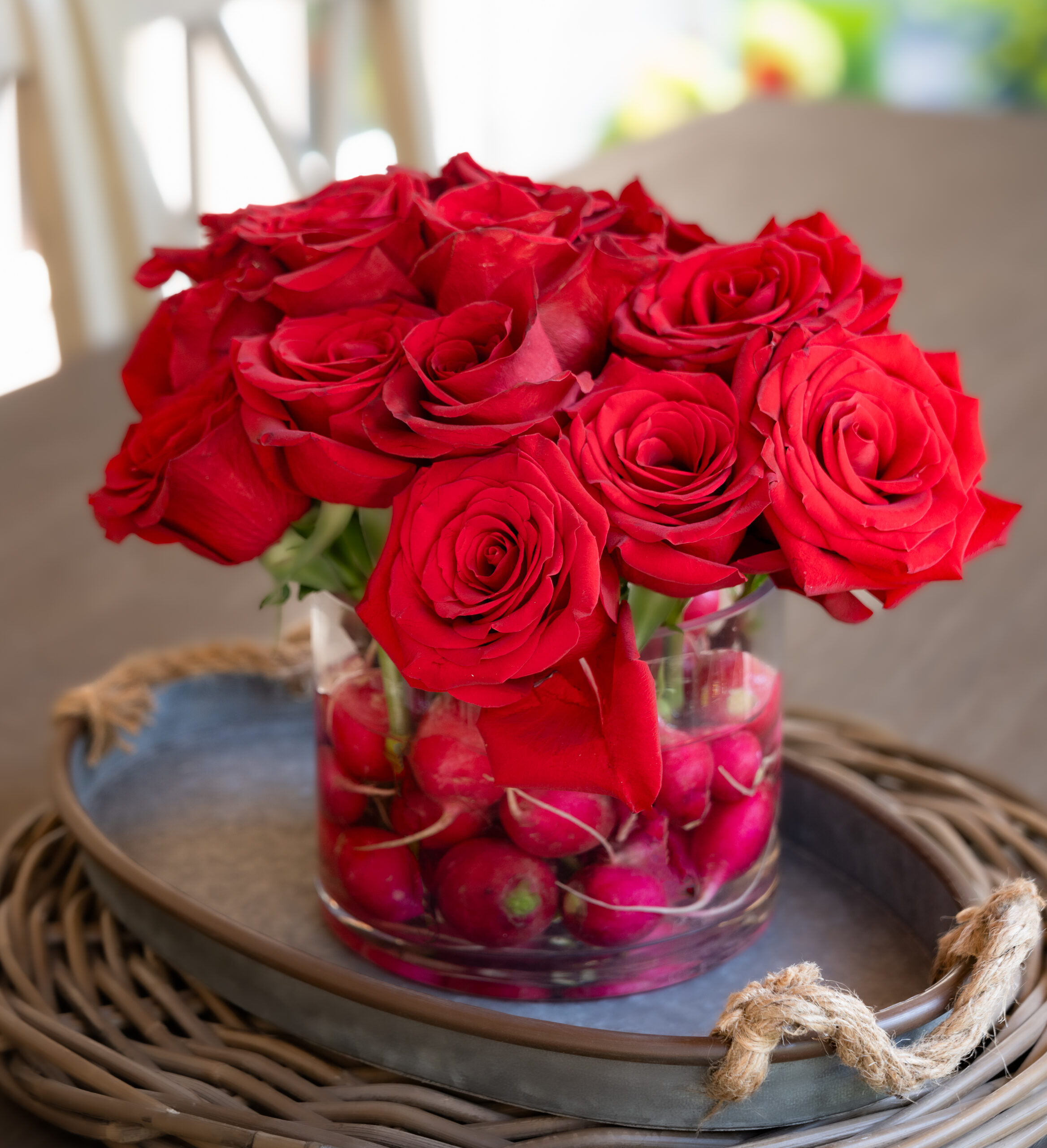 one dozen short stem roses in a clear cylinder vase with radishes inside